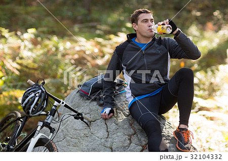 Male biker drinking water in forest 32104332