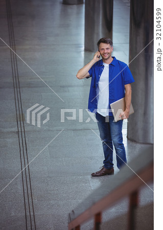 Handsome man holding laptop and talking on mobile phone Handsome man holding laptop and talking on mobile phone 32104599