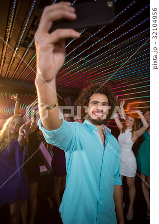 Man taking a selfie from mobile phone while friends dancing on dance floor 32104956