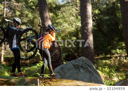 Biker couple holding their mountain bike and walking in forest 32104959
