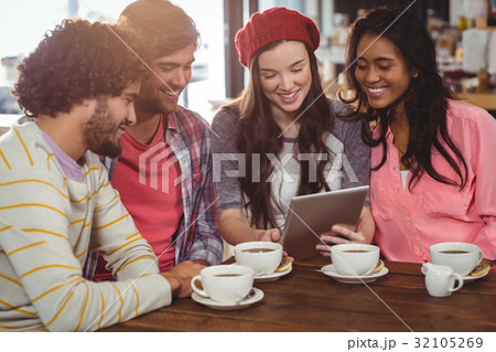 Group of friends using digital tablet while having cup of coffee Group of friends using digital tablet while having cup of coffee 32105269