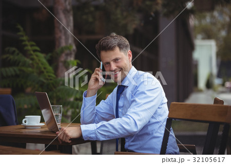 Handsome businessman talking on mobile phone while using laptop Handsome businessman talking on mobile phone while using laptop 32105617