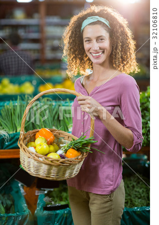 Smiling woman holding basket of vegetables in organic section 32106810