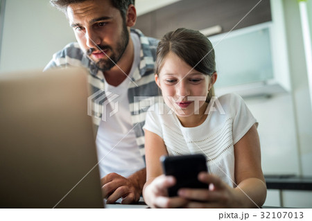 Father and daughter using laptop and mobile phone in the living room Father and daughter using laptop and mobile phone in the living room 32107013