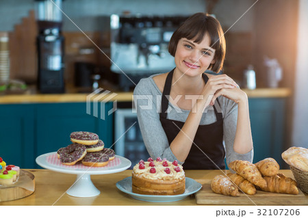 Portrait of waitress sitting at counter with sweet food on table 32107206