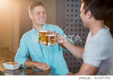 Two male friends toasting beer mugs at bar counter 32107350