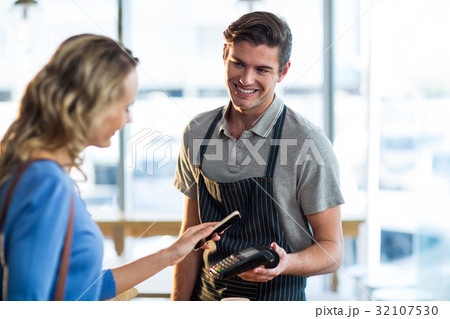 Woman paying bill through smartphone using NFC technology Woman paying bill through smartphone using NFC technology 32107530