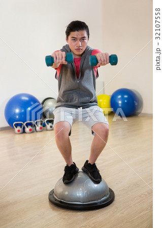Man exercising with dumbbells on bosuball Man exercising with dumbbells on bosuball 32107558