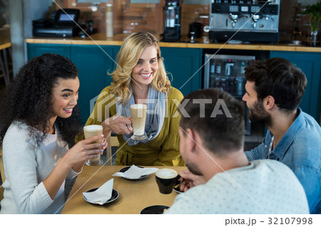 Smiling friends having a cup of coffee and cold coffee in café Smiling friends having a cup of coffee and cold coffee in café 32107998