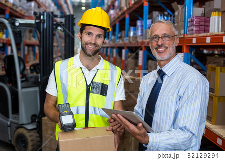 Warehouse manager holding digital tablet while male worker scanning barcode 32129294