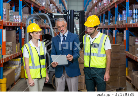 Warehouse manager and co-workers discussing over clipboard 32129339