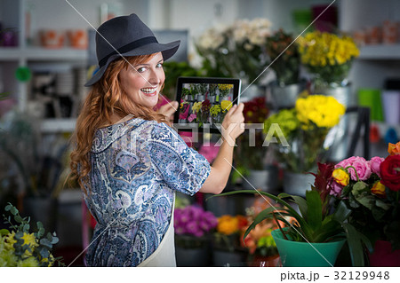 Female florist taking photograph of flowers from digital tablet in flower shop 32129948