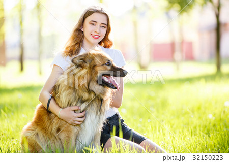 Teenage smiling girl with her dog sitting in park 32150223