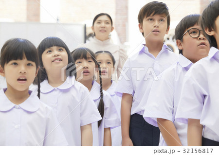 pupils and teacher are standing, looking and singing. 32156817