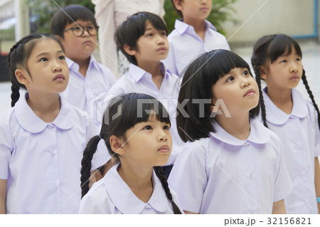 Boys and girls in uniform are standing and looking at something. 32156821