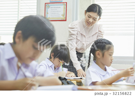 Teacher is helping a kid write something while other pupils are studying. 32156822