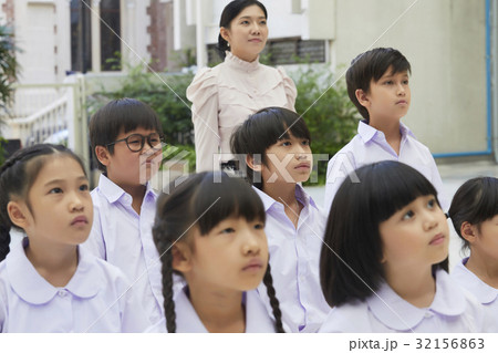 A teacher and her pupils are standing at schoolyard and looking at something. 32156863