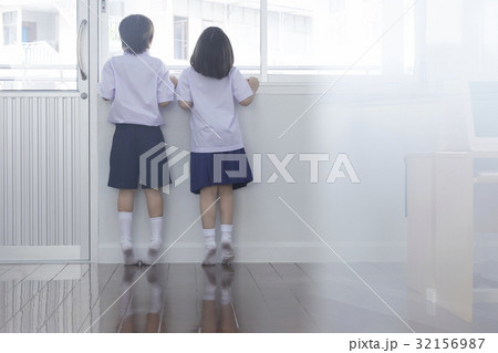 two children are standing on the toes and looking outside from window 32156987