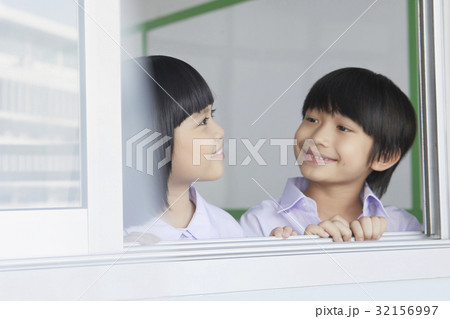 Little boy and girl are smiling and looking at each other at a window. 32156997