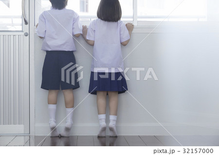 Two schoolchildren are standing on tiptoe and looking outside from window. 32157000