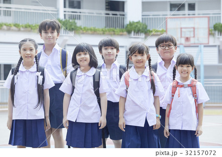A group of primary pupils is standing in lines and smiling happily outside. 32157072