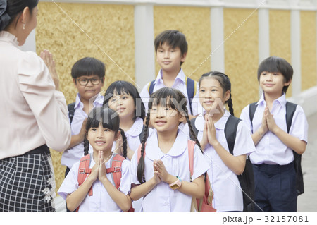 Schoolchildren and their teacher are greeting each other outside. 32157081
