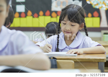 a photo of a girl sitting, smiling and writing something in a class. 32157109