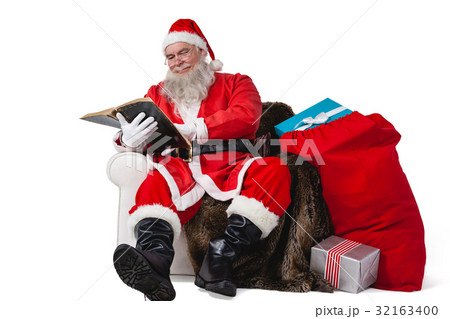 Santa reading bible with sack of christmas present beside him 32163400
