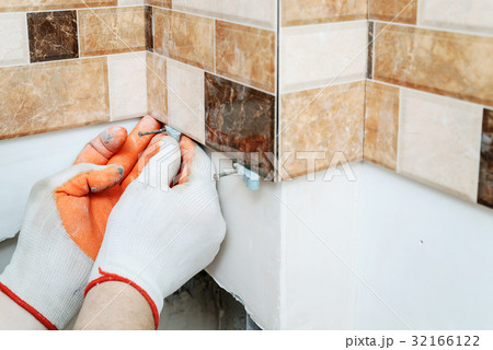 The tiler's hands are using plastic wedges. 32166122