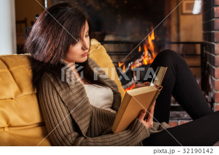 Woman reading a book by fireplace Woman reading a book by fireplace 32190142