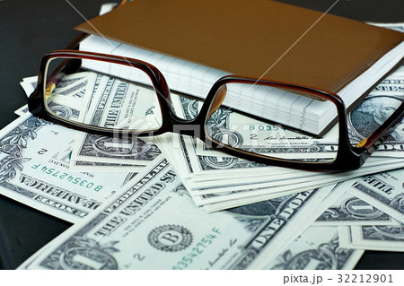 Brown glasses and small notebook on US dollar bank Brown glasses and small notebook on US dollar bank 32212901