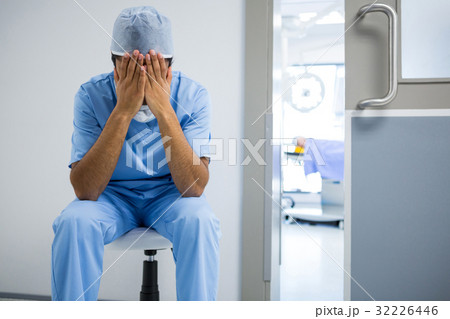 Tensed surgeon sitting with hands on face in corridor 32226446