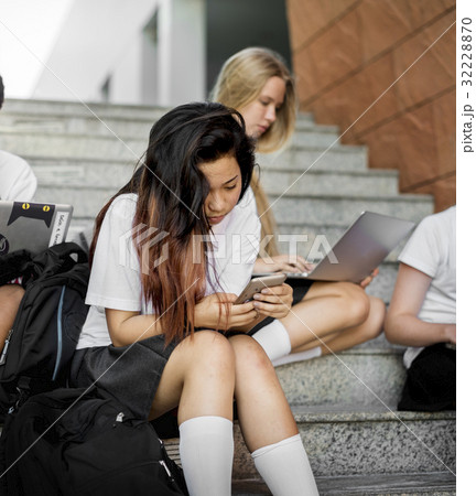 Group of students sitting at stairs and using digital devices 32228870