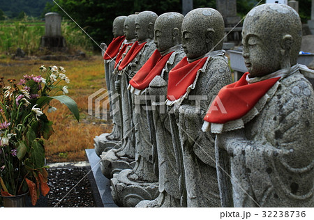 お墓の前に並ぶお地蔵様とお供えの仏花の写真素材