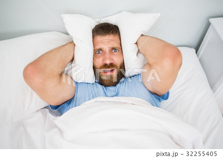 Man covering ears with pillow in bed Man covering ears with pillow in bed 32255405