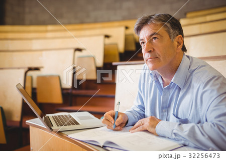 Thoughtful professor writing in book at desk Thoughtful professor writing in book at desk 32256473