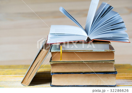 Open book, stack of hardback books on wooden table 32286626