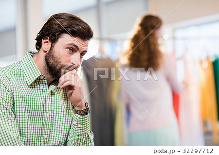 Bored man waiting his wife while woman by clothes rack 32297712