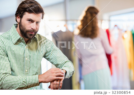 Bored man waiting his wife while woman by clothes rack Bored man waiting his wife while woman by clothes rack 32300854