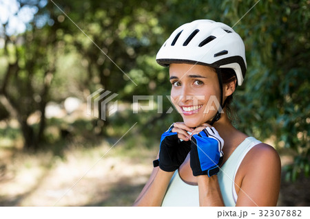 Woman smiling and fastening her cycling helmet Woman smiling and fastening her cycling helmet 32307882