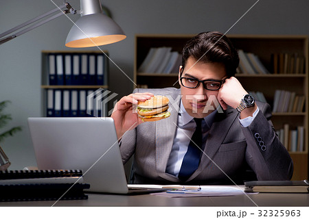 Businessman late at night eating a burger 32325963