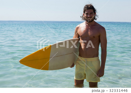 Smiling surfer with surfboard standing at beach coast Smiling surfer with surfboard standing at beach coast 32331446