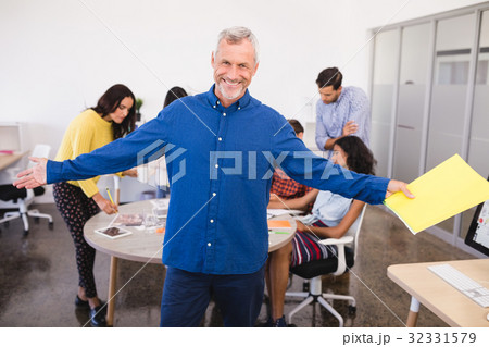 Portrait of businessman with arms outstretched with colleagues in background Portrait of businessman with arms outstretched with colleagues in background 32331579