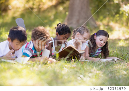 Group of friends reading book while lying on grassy field Group of friends reading book while lying on grassy field 32331979