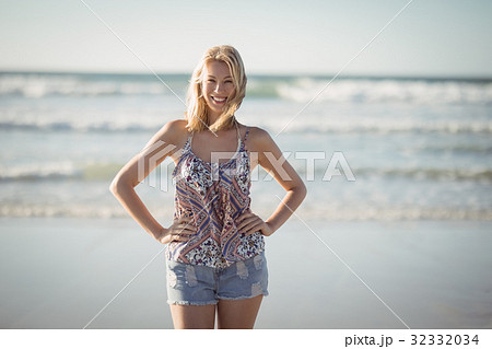 Portrait of smiling woman standing with hands on hip at beach 32332034