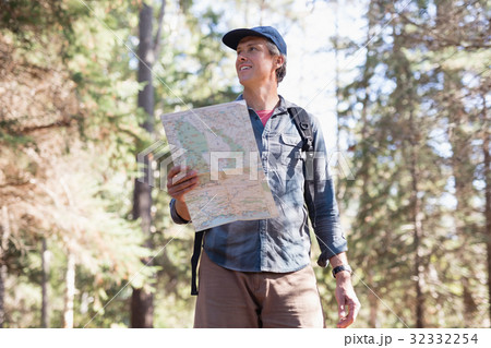 Low angle view of hiker with map standing in forest Low angle view of hiker with map standing in forest 32332254