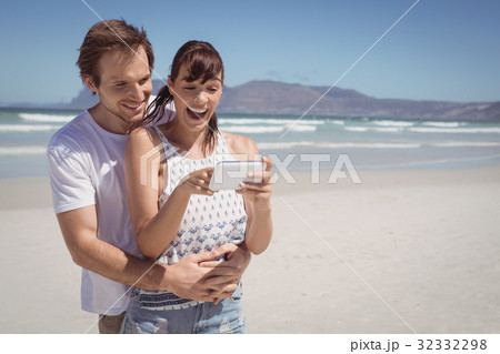 Cheerful couple using mobile phone at beach Cheerful couple using mobile phone at beach 32332298