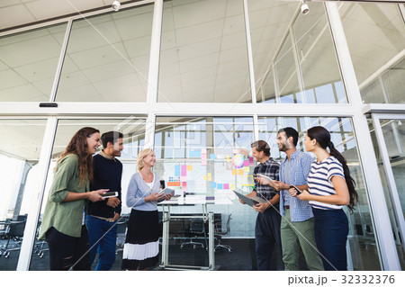 Smiling business colleagues standing against glass wall Smiling business colleagues standing against glass wall 32332376