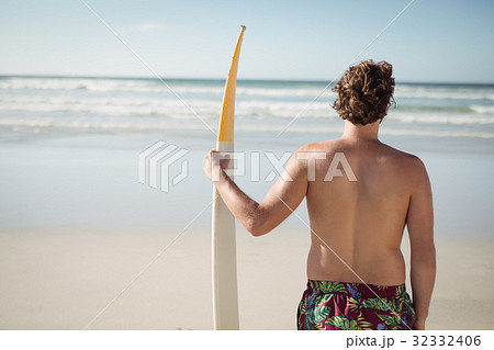 Rear view of shirtless man holding surfboard at beach 32332406