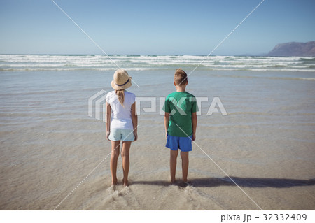 Rear view of siblings standing at beach 32332409